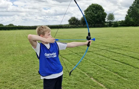 Child taking part in outdoor archery activity during Game On holiday sports course